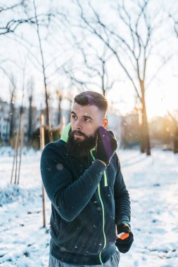 Bluetooth döneminden kalma tomurcuklarını kullanarak oldukça soğuk ve karlı bir günde dışarıda koşup egzersiz yapmaya başlamadan önce sakallı yakışıklı bir orta yaşlı adam. Spor ve spor motivasyon teması.