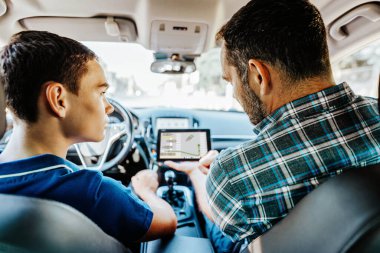 Öğrencisiyle arabada oturan bir sürücü eğitmeni. Ona temel direksiyon ve trafik kurallarını açıkla. Eğitim amaçlı olarak elektronik tablet kullanıyor. İçeriden görüntüle.
