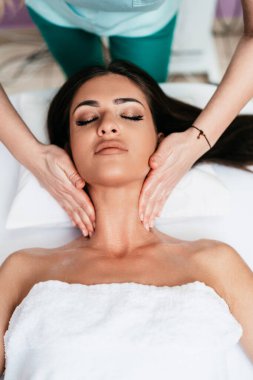 Beautiful young adult brunette receiving professional relaxation massage treatment at beauty spa salon.