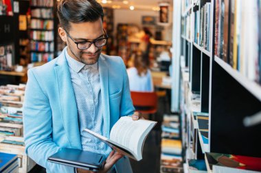 Orta yaşlı bir adam modern kitapçıda kitap seçiyor ve okuyor..