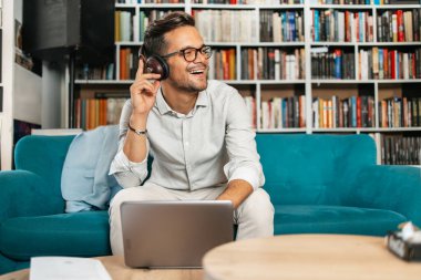 Genç, hoş görünümlü sanatçı stüdyo veya oturma odasında oturuyor, müzik dinliyor, dizüstü bilgisayarında çalışıyor, gülümsüyor ve bir sonraki başarılı projesini düşünüyor.. 