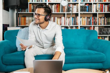 Genç, hoş görünümlü sanatçı stüdyo veya oturma odasında oturuyor, müzik dinliyor, dizüstü bilgisayarında çalışıyor, gülümsüyor ve bir sonraki başarılı projesini düşünüyor.. 