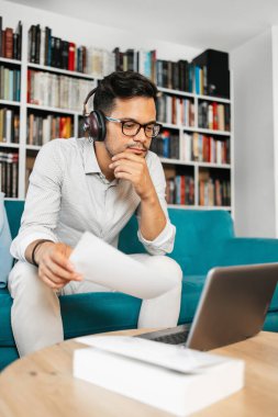 Genç, hoş görünümlü sanatçı stüdyo veya oturma odasında oturuyor, müzik dinliyor, dizüstü bilgisayarında çalışıyor, gülümsüyor ve bir sonraki başarılı projesini düşünüyor.. 