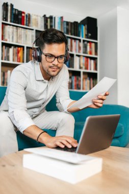 Genç, hoş görünümlü sanatçı stüdyo veya oturma odasında oturuyor, müzik dinliyor, dizüstü bilgisayarında çalışıyor, gülümsüyor ve bir sonraki başarılı projesini düşünüyor.. 