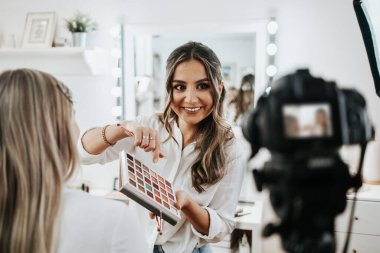 Evden ya da atölyeden güzel makyaj videosu yayınlayan mutlu genç bir kadın. Güzel çevrimiçi içerik kozmetikçisi makyaj yapıyor ve bazı iş araçlarını açıklıyor. Günlük kaydı ve çevrimiçi kanal çalışması. 
