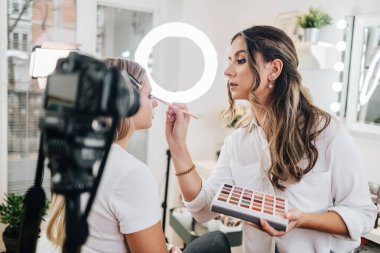 Evden ya da atölyeden güzel makyaj videosu yayınlayan mutlu genç bir kadın. Güzel çevrimiçi içerik kozmetikçisi makyaj yapıyor ve bazı iş araçlarını açıklıyor. Günlük kaydı ve çevrimiçi kanal çalışması. 