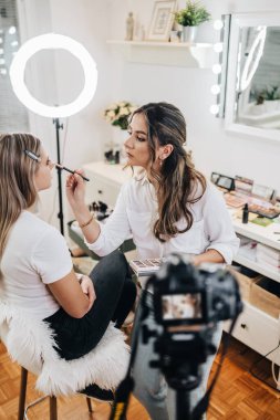 Evden ya da atölyeden güzel makyaj videosu yayınlayan mutlu genç bir kadın. Güzel çevrimiçi içerik kozmetikçisi makyaj yapıyor ve bazı iş araçlarını açıklıyor. Günlük kaydı ve çevrimiçi kanal çalışması. 