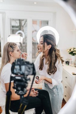 Evden ya da atölyeden güzel makyaj videosu yayınlayan mutlu genç bir kadın. Güzel çevrimiçi içerik kozmetikçisi makyaj yapıyor ve bazı iş araçlarını açıklıyor. Günlük kaydı ve çevrimiçi kanal çalışması. 