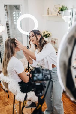 Evden ya da atölyeden güzel makyaj videosu yayınlayan mutlu genç bir kadın. Güzel çevrimiçi içerik kozmetikçisi makyaj yapıyor ve bazı iş araçlarını açıklıyor. Günlük kaydı ve çevrimiçi kanal çalışması. 