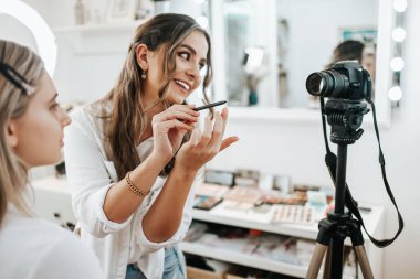 Evden ya da atölyeden güzel makyaj videosu yayınlayan mutlu genç bir kadın. Güzel çevrimiçi içerik kozmetikçisi makyaj yapıyor ve bazı iş araçlarını açıklıyor. Günlük kaydı ve çevrimiçi kanal çalışması. 