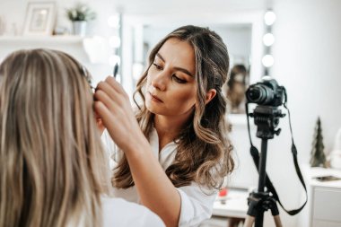 Evden ya da atölyeden güzel makyaj videosu yayınlayan mutlu genç bir kadın. Güzel çevrimiçi içerik kozmetikçisi makyaj yapıyor ve bazı iş araçlarını açıklıyor. Günlük kaydı ve çevrimiçi kanal çalışması. 