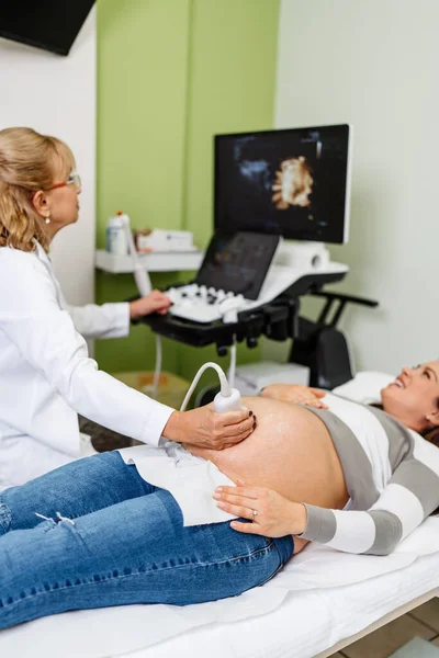 Female doctor doing ultrasound scan for a beautiful pregnant woman. Side view. Modern pregnancy  and healthcare concept.