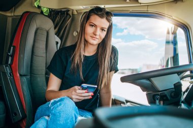 Profesyonel kamyon şoförünün uzun bir yolculuktan sonra oturup dinlendiği güzel bir kadın portresi. Çevrimiçi iletişim için akıllı telefonunu kullanıyor. Aracın içinde. İnsanlar ve ulaşım kavramı.