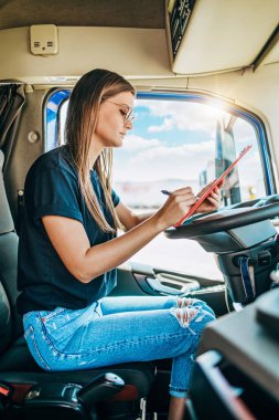 Profesyonel kamyon şoförünün uzun bir yolculuktan sonra oturup dinlendiği güzel bir kadın portresi. Not defterine bir şeyler yazıyor. Aracın içinde. İnsanlar ve ulaşım kavramı.