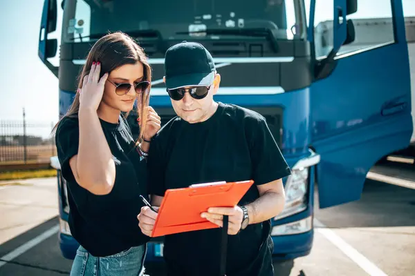 Two professional truck drivers stand in front of the big truck. They talk and perform a technical inspection of the vehicle before next drive. Professional transportation concept.