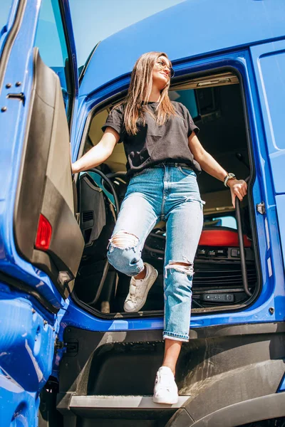 Portrait of beautiful young woman professional truck driver standing on truck cabin doors. People and transportation concept.