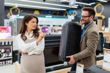 Beautiful and happy middle age couple buying consumer tech products in modern home appliances store. They are choosing home theater and TV devices. People and consumerism concept.