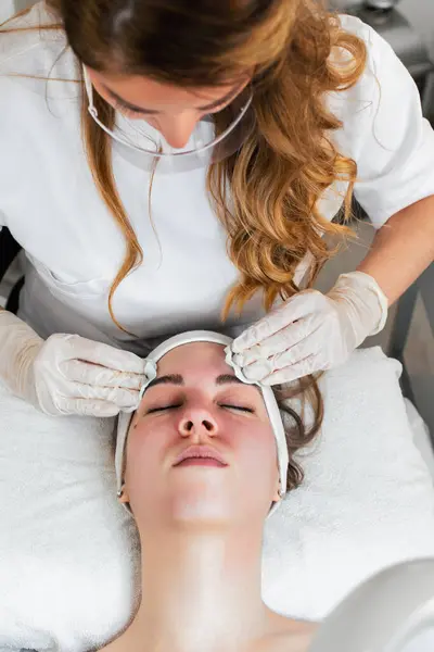 Young woman receiving face lift treatment with high-frequency wand. This modern treatment uses electric currents to kill acne-causing bacteria, reduce inflammation, and improve skin tone and texture.