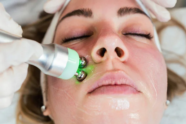 Young woman receiving modern facial low-voltage electrical treatment to stimulate elastin and collagen production for facial muscles improvement. Most popular face lifting treatment. Cosmetician work.