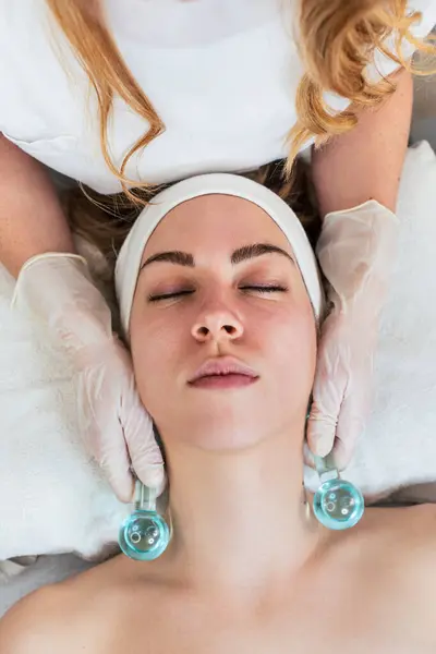 Beautiful young woman enjoying in cryotherapy with cryo sticks or ice globes. Modern and popular beauty procedure for reducing redness, inflammation and skin puffiness. Skincare treatment concept.