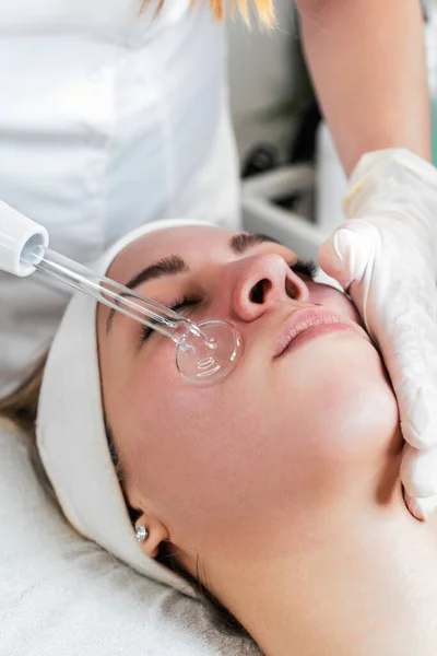 Young woman receiving face lift treatment with high-frequency wand. This modern treatment uses electric currents to kill acne-causing bacteria, reduce inflammation, and improve skin tone and texture.