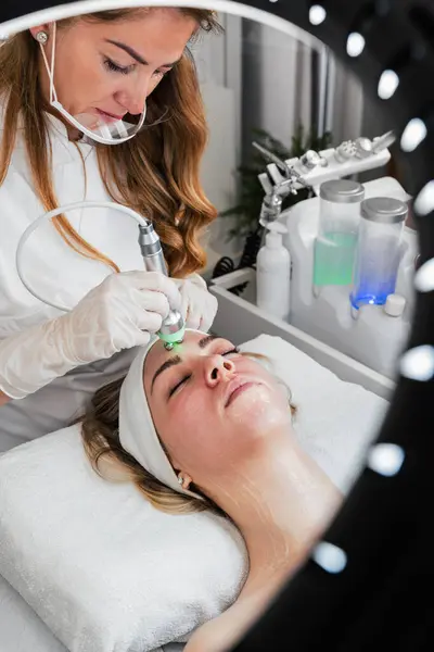 Young woman receiving modern facial low-voltage electrical treatment to stimulate elastin and collagen production for facial muscles improvement. Most popular face lifting treatment. Cosmetician work.