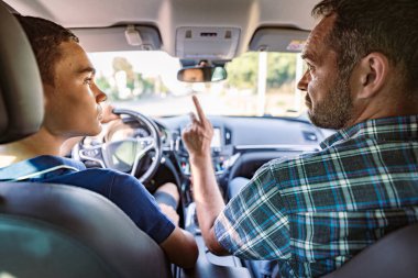 Öğrencisiyle arabada oturan bir sürücü eğitmeni ve ona temel direksiyon kurallarını, trafik kurallarını ve kendini sürüş için nasıl doğru dürüst hazırlaması gerektiğini anlatıyor. İçeriden görüntüle.