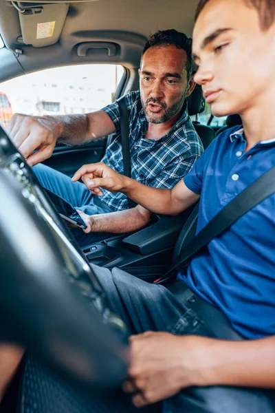 Driving instructor sitting in a car with his student and explain to him driving basics, traffic rules and how to properly prepare himself for a drive. View from inside.