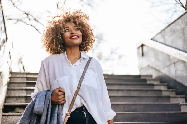 美丽时髦的黑人妇女站在地铁站 她很高兴 用她的智能手机和别人说话 公共交通和城市生活概念 免版税图库照片