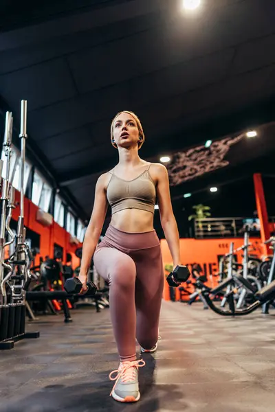 Beautiful skinny redhead woman exercising in a spacious and modern equipped fitness gym. People and recreation concept.