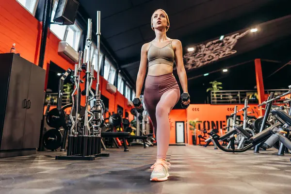 Beautiful skinny redhead woman exercising in a spacious and modern equipped fitness gym. People and recreation concept.
