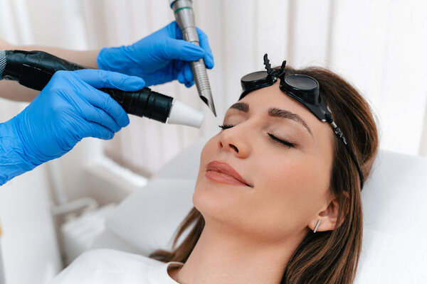 Beauty laser expert doing a cosmetic skin resurfacing treatment on a beautiful female patient. Modern and popular anti age procedure for removing old and stimulating new tissue creation.