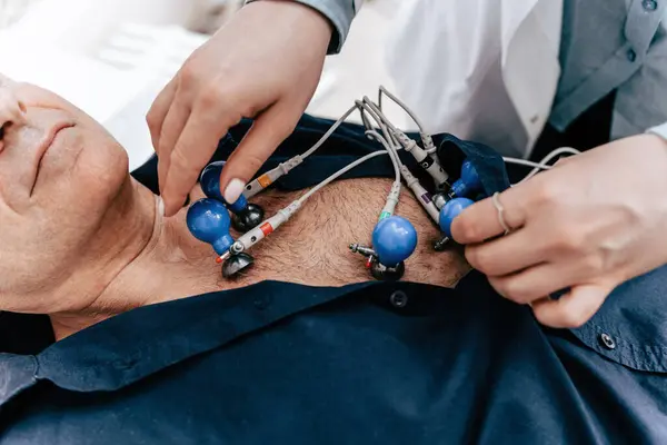 有经验的医生把心电图机的电极放在老年男性病人的裸体上 在医院的急诊室近距离拍摄 图库照片