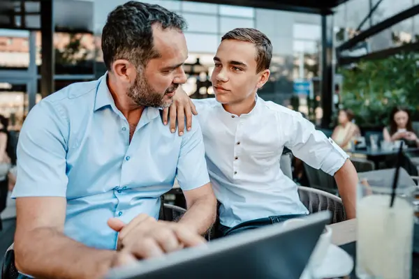 英俊快乐的父亲和他十几岁的儿子坐在餐馆里聊天 图库图片