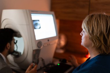 Güzel kadın doktor göz doktoru modern klinikteki yakışıklı orta yaşlı adamın görüşünü kontrol ediyor. Göz hekimliği kliniğinde doktor ve hasta kontrolü sırasında..