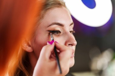 Profesyonel güzellik uzmanı güzel genç bir kadının yüzüne makyaj yapıyor. Muhteşem bir kadın modelle profesyonel makyaj stüdyosu çalışması..