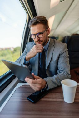 Hızlı trenle seyahat ederken elektronik tabletini kullanan orta yaşlı yakışıklı bir işadamı. Modern ve hızlı seyahat kavramı.