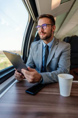 Hızlı trenle seyahat ederken elektronik tabletini kullanan orta yaşlı yakışıklı bir işadamı. Modern ve hızlı seyahat kavramı.