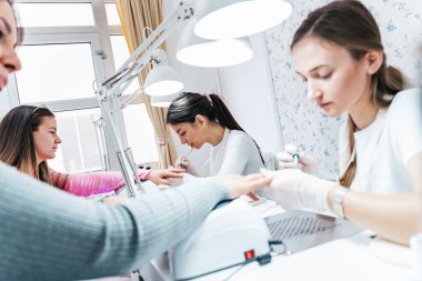 Modern bir güzellik salonunda çalışan profesyonel manikürcüler. Tatmin olmuş kadın müşteriler kaplıca merkezinde manikür tedavisi görüyor..