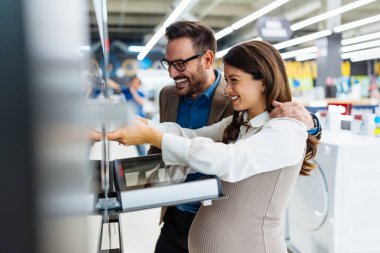 Beautiful and happy middle age couple buying consumer tech products in modern home appliances store. They are choosing electrical cooker and oven. People and consumerism concept.