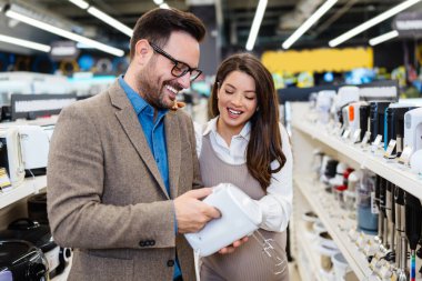 Beautiful and happy middle age couple buying consumer tech products in modern home tech store. They are choosing small kitchen appliances. People and consumerism concept.