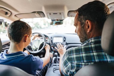 Öğrencisiyle arabada oturan bir sürücü eğitmeni ve ona temel direksiyon kurallarını, trafik kurallarını ve kendini sürüş için nasıl doğru dürüst hazırlaması gerektiğini anlatıyor. İçeriden görüntüle.