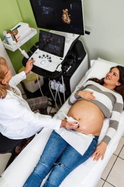 Female doctor doing ultrasound scan for a beautiful pregnant woman. Side view. Modern pregnancy and healthcare concept.