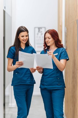 İki güzel ve ciddi kadın doktor ya da modern bir klinikte göz hastalıklarının teşhisi ve tedavisi için duran ve belge okuyan bir teknisyen. Sağlık ve Tıp Konsepti.