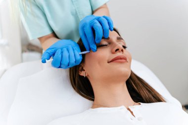 Çekici kadın güzellik kliniğinde gençleştirici yüz enjeksiyonu yaptırıyor. Güzellik uzmanı kadın kırışıklıklarını botulinyum toksin iğneleriyle ya da hyaluronik asit doldurucularıyla dolduruyor..