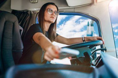 Genç ve güzel bir kadının portresi. Profesyonel kamyon şoförü oturuyor ve büyük bir kamyon sürüyor. Aracın içinde. İnsanlar ve ulaşım kavramı.