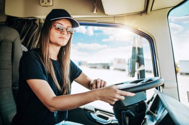 Büyük bir kamyonda oturan ve kameraya bakan genç ve güzel bir kadın kamyon şoförünün portresi. Aracın içinde. İnsanlar ve ulaşım kavramı.