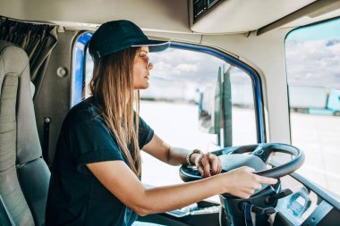 Genç ve güzel bir kadının portresi. Profesyonel kamyon şoförü oturuyor ve büyük bir kamyon sürüyor. Aracın içinde. İnsanlar ve ulaşım kavramı.