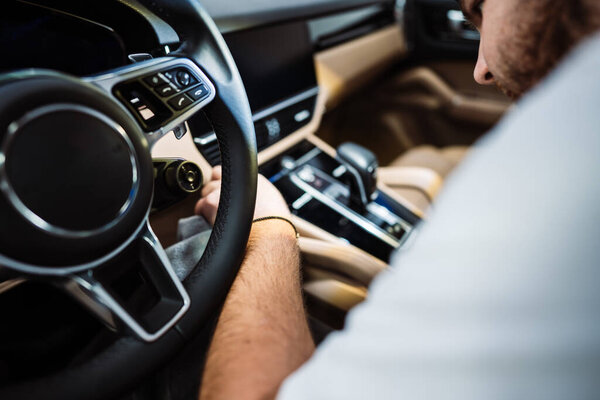 Мужчина очищает интерьер роскошного автомобиля с помощью ткани из микроволокна, автомобильной детализации или концепции парковки. Селективный фокус.