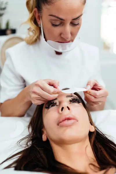 stock image Beautiful young adult woman receiving professional eyelash makeup treatment. Cosmetician is smiling and looking at camera. Beauty and cosmetics business. 